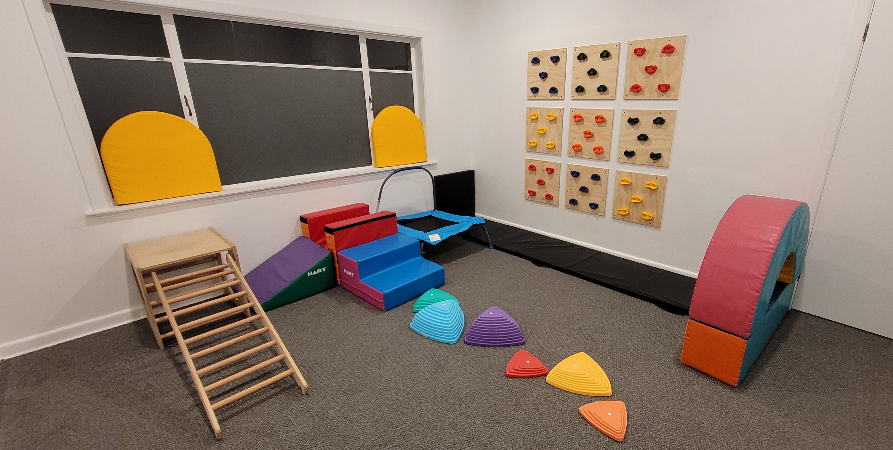 Resilient Kids OT clinic therapy room with climbing wall, soft-play equipment, balance stepping stones and a trampoline